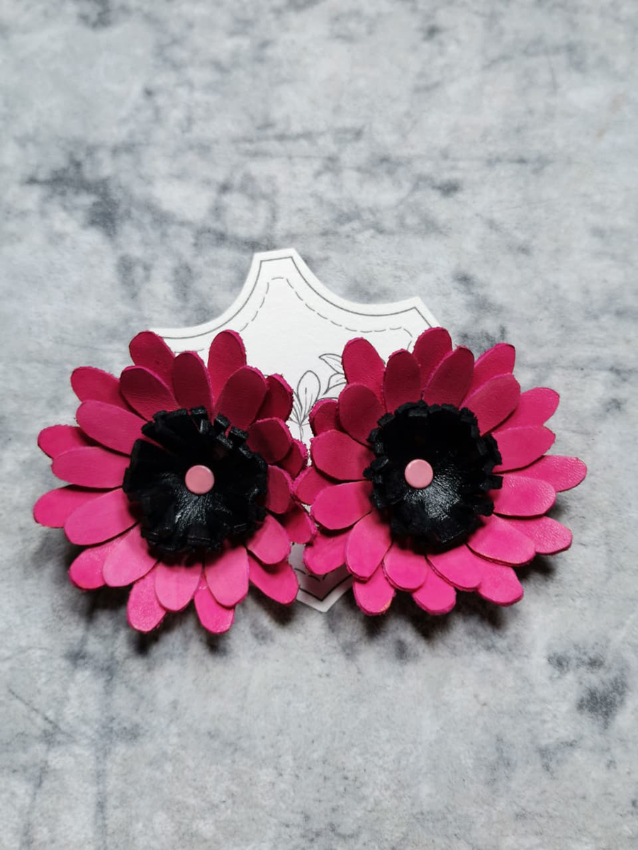 Par de aros artesanales en forma de flor, elaborados en cuero fucsia con centro negro, presentados sobre superficie clara.
