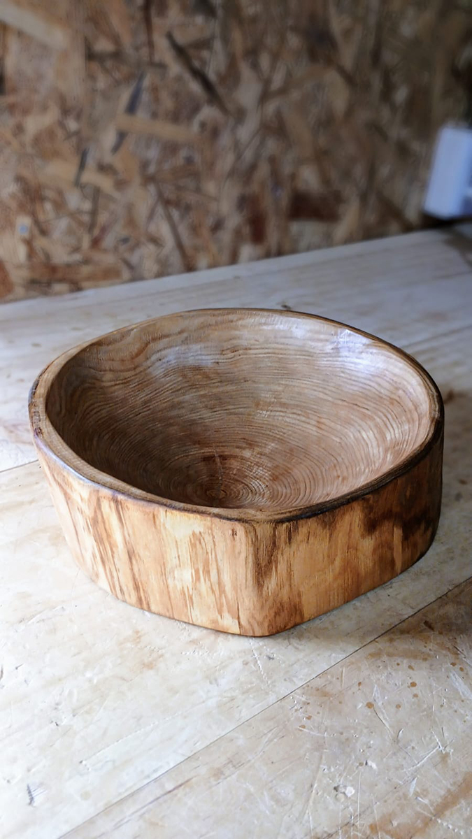 Cuenco artesanal de madera maciza, tallado a mano, con vetas naturales visibles y acabado liso, apoyado sobre una mesa de trabajo.