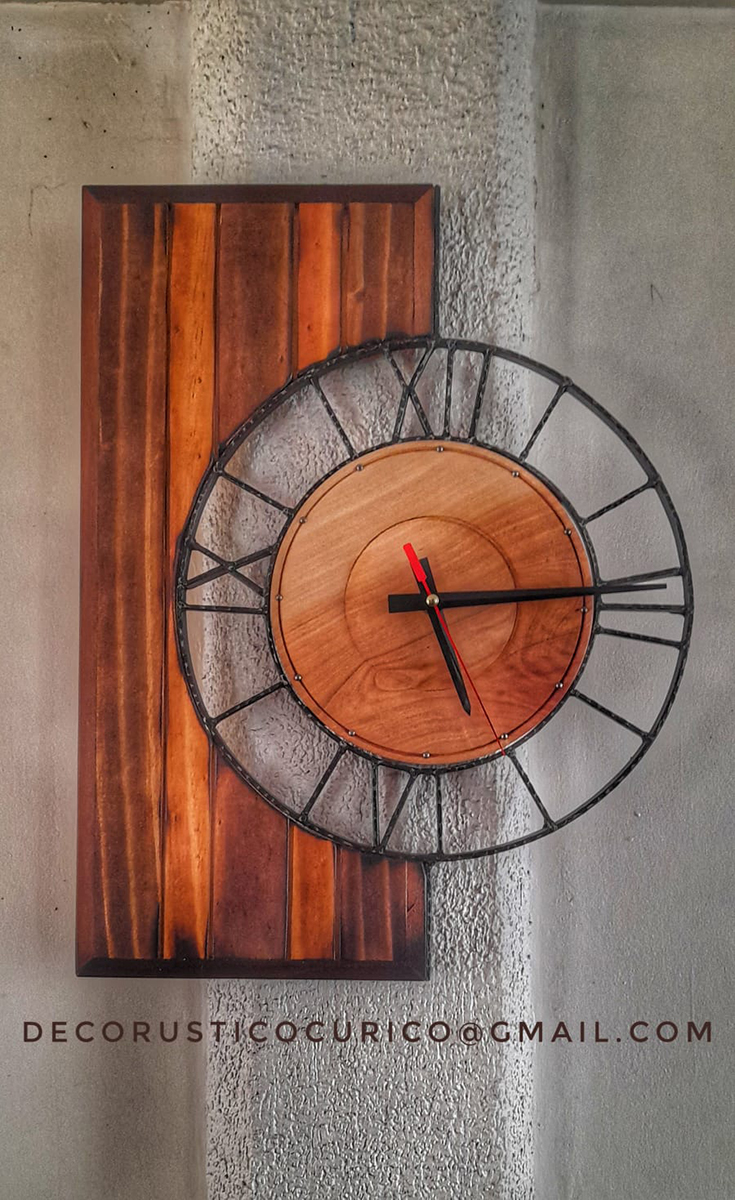 Reloj de pared con estructura circular de hierro y centro de madera natural montado sobre panel vertical de madera.