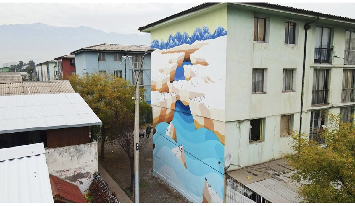Mural de gran formato pintado en el costado de un edificio de departamentos, con formas abstractas que evocan montañas y agua en tonos azules, beige y blanco.