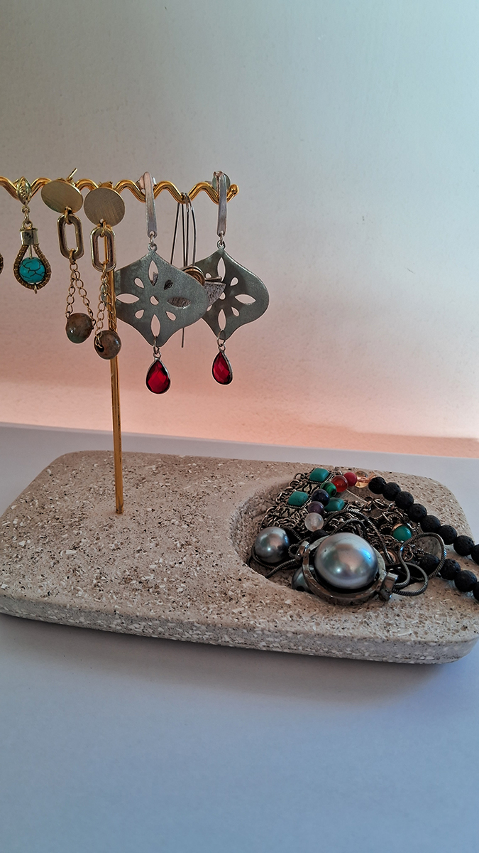Soporte para aros con base de piedra y joyas metálicas exhibidas, acompañado de accesorios sobre la superficie.